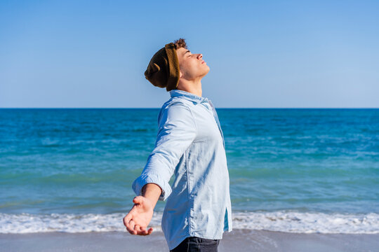 Man wearing knit hat standing with arms outstretched on sunny day at beach