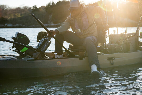 Man getting out of his fishing kayak at sunset