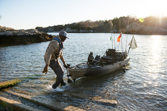 Man launches his fishing kayak from a rocky shore