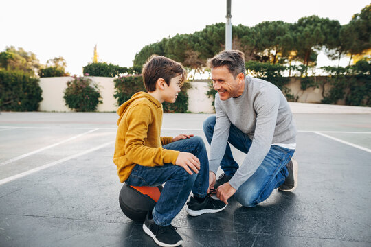 Father lacing son's shoe on basketball outdoor court