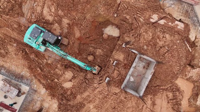Top Down Drone View of Excavator Digging Foundation Pit. Overhead drone footage of a turquoise excavator digging a new foundation pit in orange clay soil.