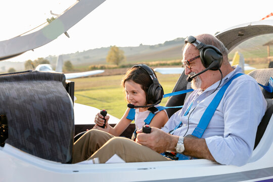 Granddaughter sitting with grandfather inside airplane at airfield