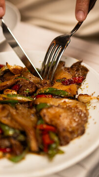 Close-up action shot of Turkish chicken saut&eacute; with green and red peppers, mushrooms being cut with fork and knife, rich caramelized flavors, authentic Turkish tavuk kavurma dish.