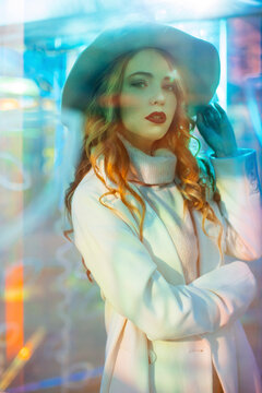 Fashion model in coat poses behind glass with neon glow