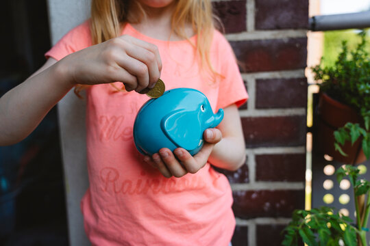 Hands of girl saving coin in piggy bank
