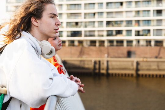 Youth in hoodie leaning on railing at HafenCity showing friendship