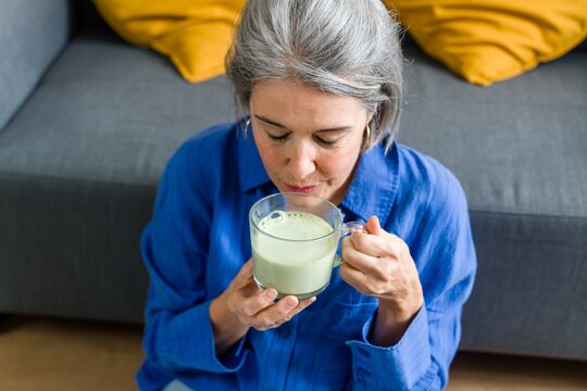 A woman smells a mug of matcha tea indoors