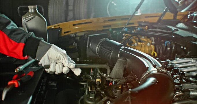 Slow motion shot of mechanic working on car engine with camera movement above engine, dramatic lighting in workshop. Automotive repair concept, maintenance and service.