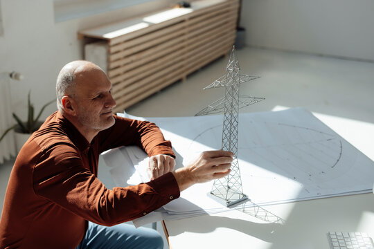 Businessman examining electricity pylon model on blueprint at desk