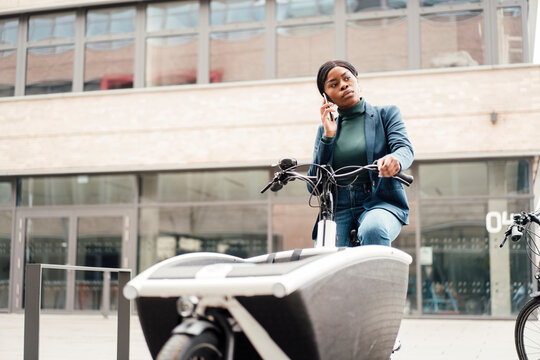 Businesswoman talking through smart phone sitting on cargo bike