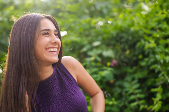 Girl smiling outdoors in a sunny green garden wearing a purple top