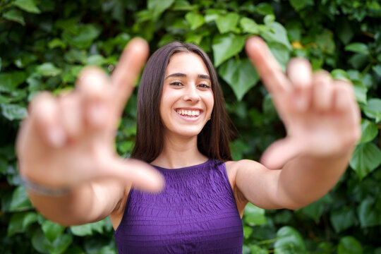 Smiling model making a framing gesture outdoors in a green garden