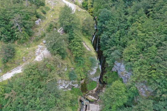 Aerial view of a waterfall cascading through a lush green forest in the mountains of Prati di Tivo, Abruzzo, Italy.