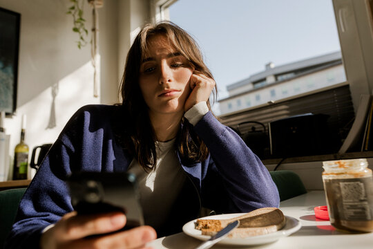 Bored woman using a smartphone at breakfast table indoors