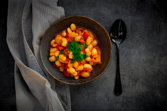 Bowl of homemade bean stew with parsley on black concrete