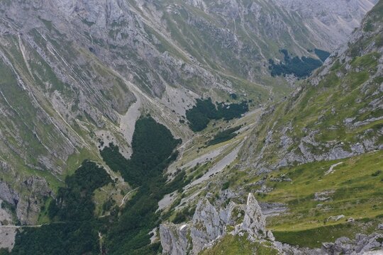 Aerial view of the rugged mountain valley of Prati di Tivo with steep rocky slopes, green alpine meadows, and dense forest patches in Prati di Tivo, Abruzzo, Italy.