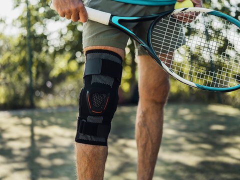 Tennis player wearing knee brace holding racket and ball outdoors