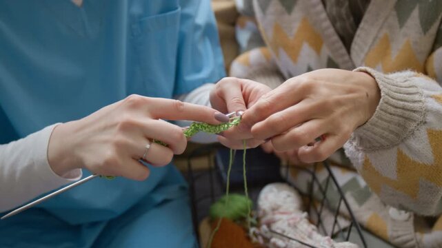 Close up shot of unrecognizable senior woman teaching young nurse knitting in retirement home. Video for senior care services and nursing home marketing