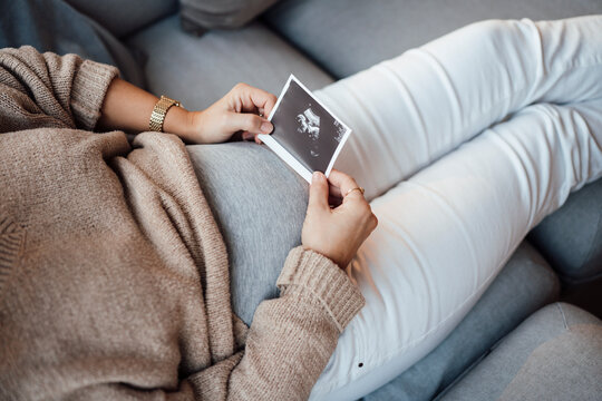 Pregnant woman holding ultrasound photo at home