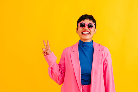 Playful young woman wearing sunglasses gesturing against colored background