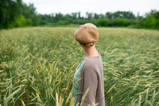 Young woman standing in a summer wheat field wearing a vintage dress and beret