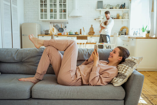 Smiling woman using mobile phone while man carrying daughter in kitchen at home