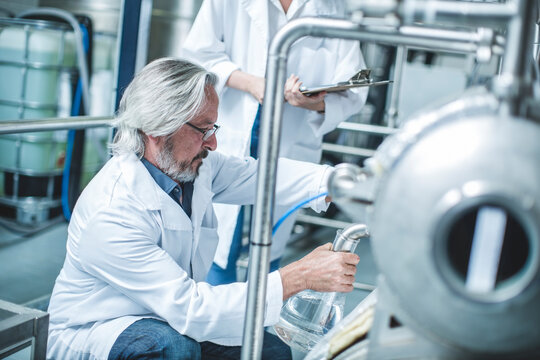 Distllers holding measuring flasks in distillery