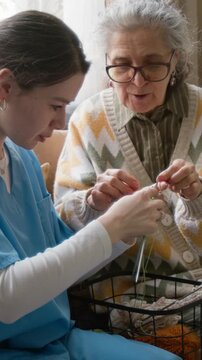 Vertical shot of young female nurse learning knitting from senior woman. Clip for assisted living and senior care marketing