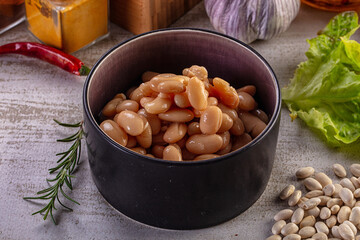 Fototapeta premium Bowl of cooked white beans with fresh herbs and spices on rustic surface