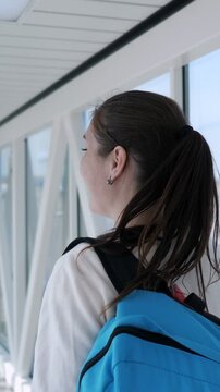 Beautiful young woman with a backpack walking down the jet bridge to board an airplane, smiling happily over her shoulder as she anticipates her vacation and new adventure