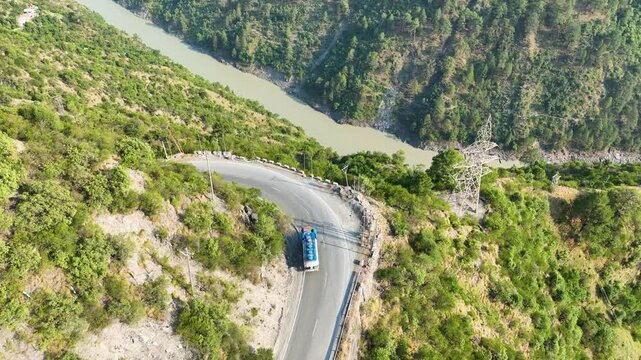 High altitude aerial of vehicles on narrow road carved into steep mountain gorge.