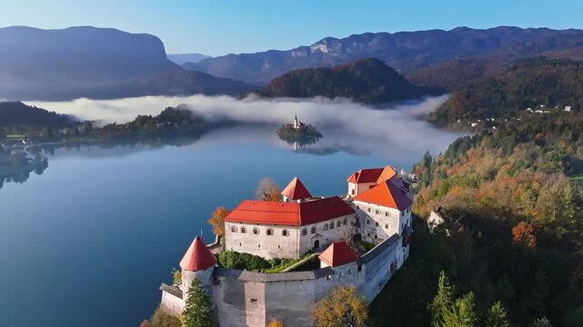 Bled, Slovenia - 4K Flying over the famous Bled Castle (Blejski Grad) towards Bled Lake on a sunny, foggy autumn morning