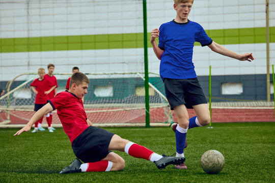 Boy sliding for soccer ball during youth match. Concept of junior football action, defensive tackle training, school sports competition, resilience lessons and team ads.