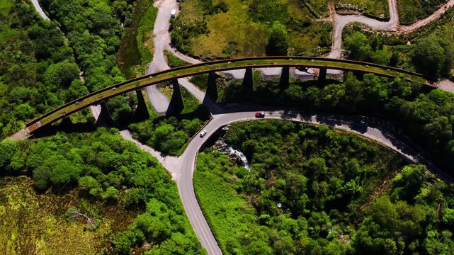 Aerial View of The Gleensk Viaduct Bridge Surrounded by Forest With a Winding Road and Cars Crossing a One Way Rural Bridge