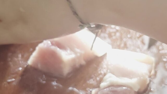 A high-quality macro close-up video capturing a person dicing fresh raw pork belly meat into uniform pieces using a sharp kitchen knife on a wet wooden cutting board sprinkled with salt