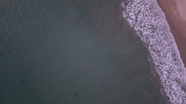 Top-down drone view captures the Pacific Ocean meeting Malibu beach in vivid sunset transition, water and sand divided in graphic abstract overhead from California coast.