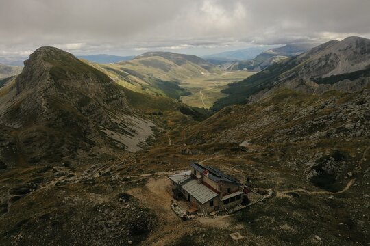 Aerial view of Piani Di Pezza valley with a mountain hut in the foreground, surrounded by rugged mountain slopes and green meadows in Rocca di Mezzo, Abruzzo, Italy.