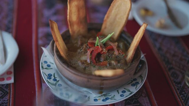 Traditional llama casserole served in an earthenware pot with crispy potato wedges, rich broth and regional ingredients rooted in Andean culinary traditions, slow motion reveal shot.