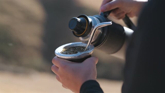 Hot water poured into a yerba mate gourd outdoors in Argentina, featuring traditional preparation, social customs and South American beverage culture, close-up shot.