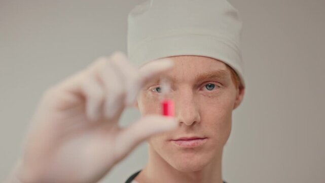Caucasian technician holding red ampoule closeup, gloved hand showcasing bloodlike sample, laboratory atmosphere, focus
