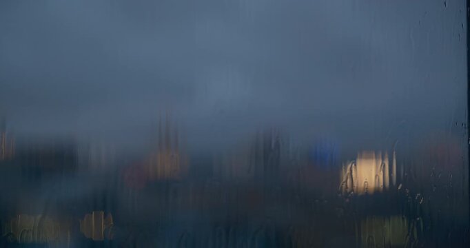 Cinematic artistic abstract city lights viewed through rain-covered window glass. Beautiful bokeh effect with blurred urban evening scene, water droplets, and condensation creating dreamy atmospheric 