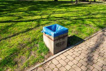 Naklejka premium Trash bin placed in a green park on grass, showing urban cleanliness infrastructure in a public outdoor recreational area during daytime with natural environment surroundings