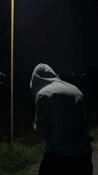 Vertical 4K slow motion rotating camera medium shot from behind of a male athlete in hoodie doing shadow boxing training under street light lamp posts at dark night Sport fitness broll