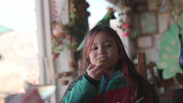 Young girl enjoys a piece of homemade bread while dining in a rustic restaurant, capturing authentic family travel and regional culinary traditions, slow motion close-up shot.