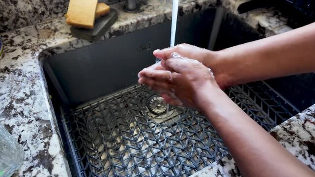 Hygiene and health are critical concepts as a South Asian person washes their hands thoroughly under running water in a kitchen sink. This action promotes sanitation, cleanliness