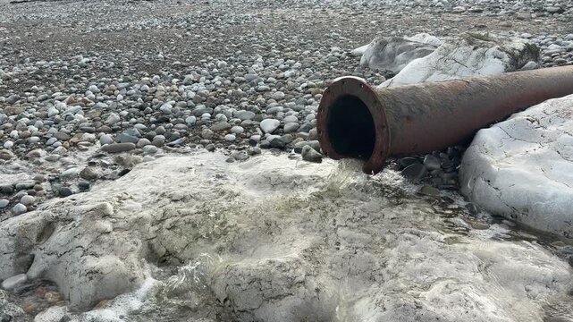 Run off water going down a pipe on to pebbles on a beach rain and pollution from farm run off UK 4K