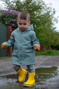 Toddler in yellow rain boots splashing in puddle Copy Space