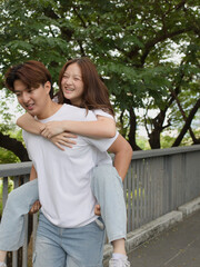 Fototapeta premium Happy Young Asian Couple Enjoying Piggyback Ride in Benchakitti Park