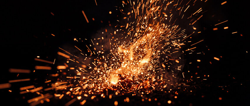 A panoramic abstract background of bright orange fire sparks and burning embers exploding rapidly in a dark black space