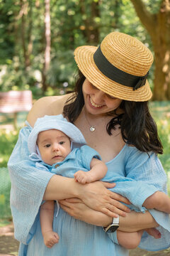 Smiling mother holding baby in sunny park portrait
